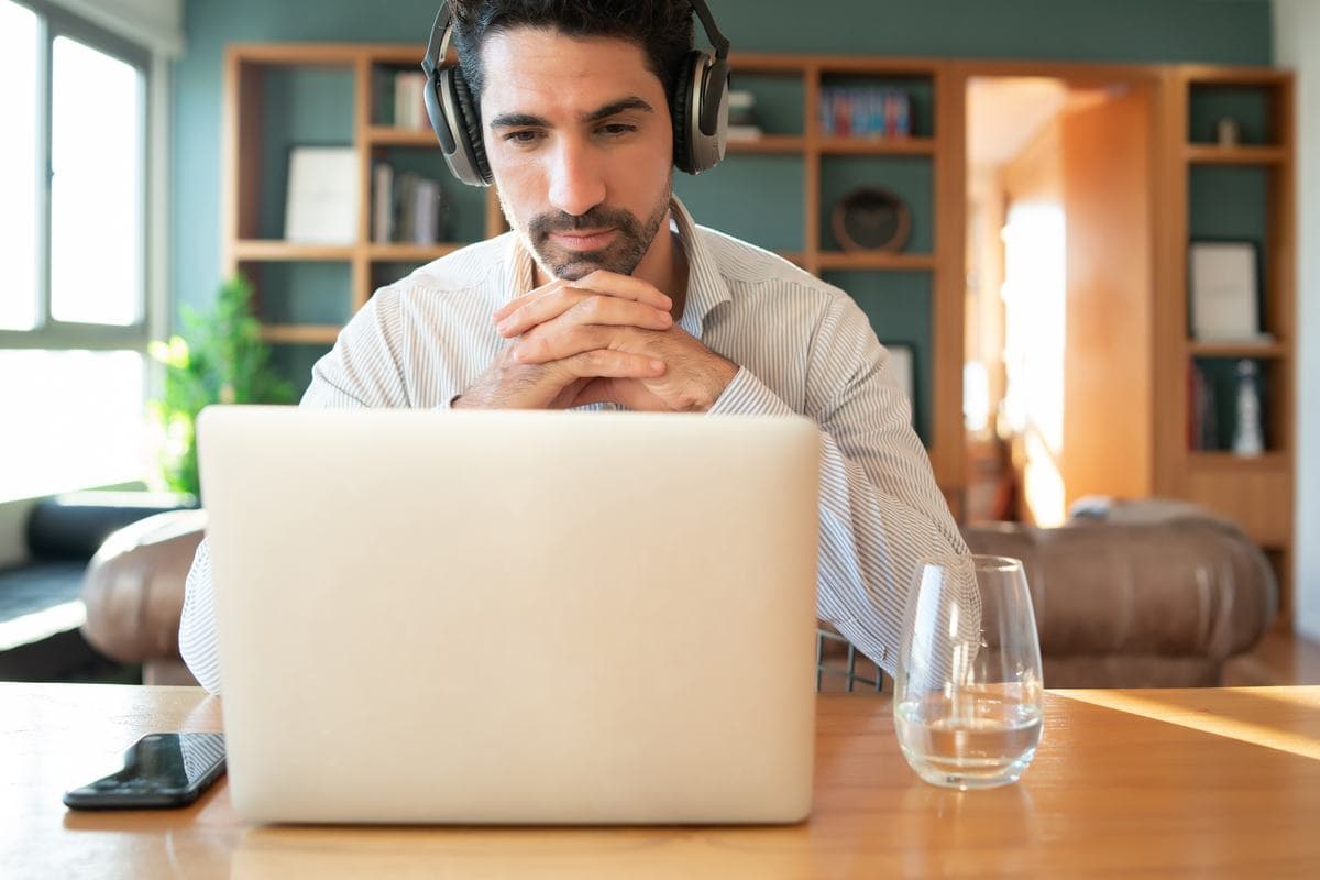 A man wearing headphones at a laptop, mid-conversation