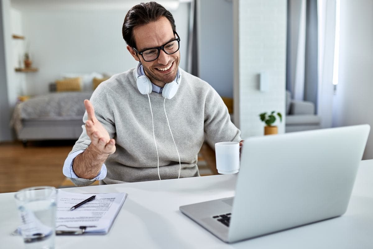 A man with headphones round his neck talking to his laptop